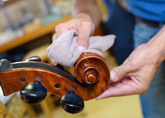 Manos limpiando con un paño suave la voluta y las clavijas de un instrumento de cuerda