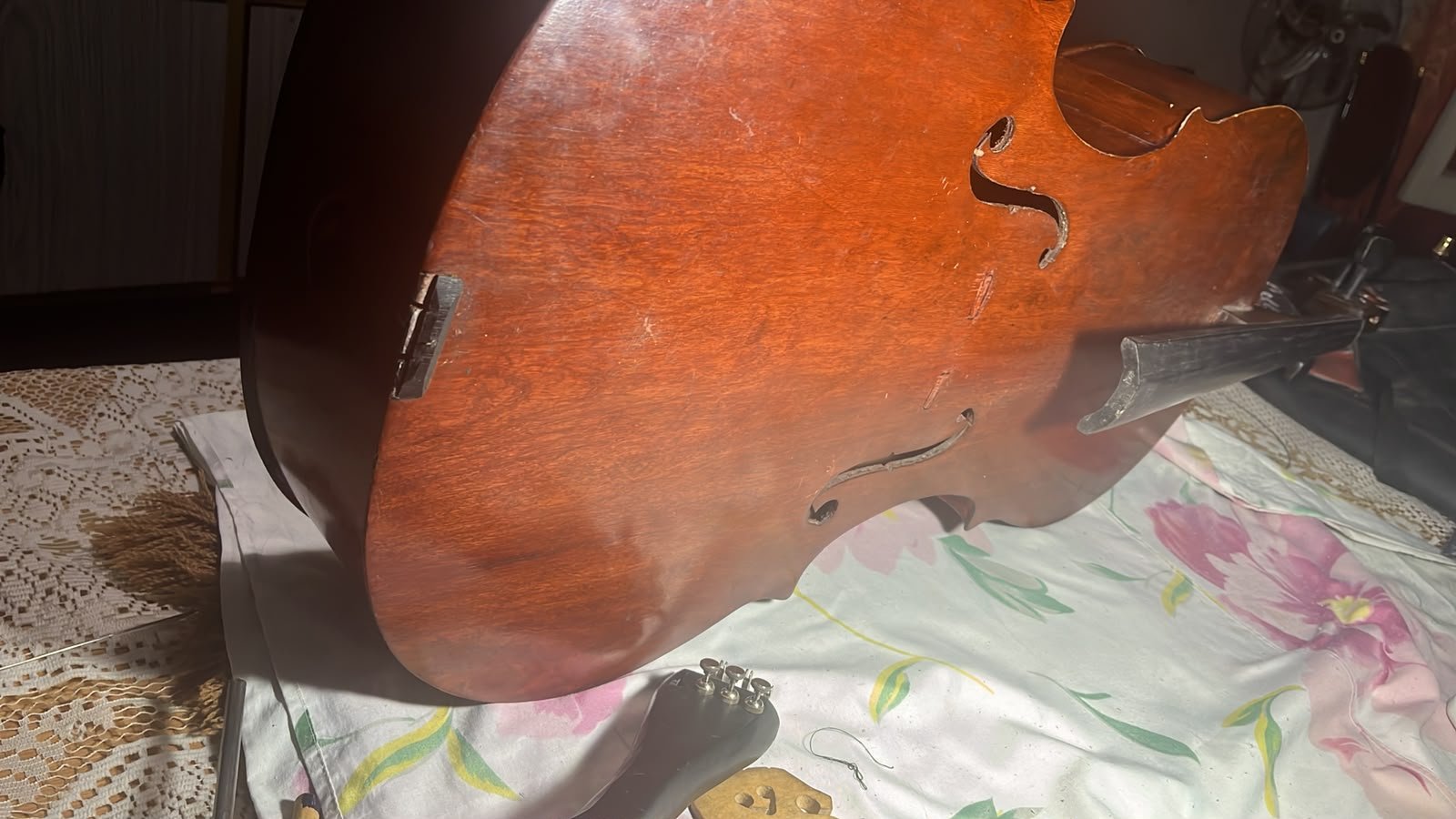 Perfil de un violonchelo de fabricación irregular, con efes asimétricas entre sí y un parche metálico tosco en el borde de la tapa