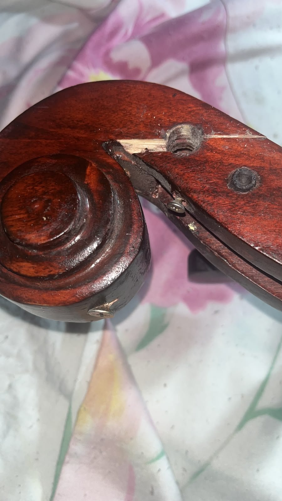 Voluta de un violonchelo de fabricación artesanal irregular, con un tornillo metálico atravesando la madera junto a una grieta reparada de forma tosca